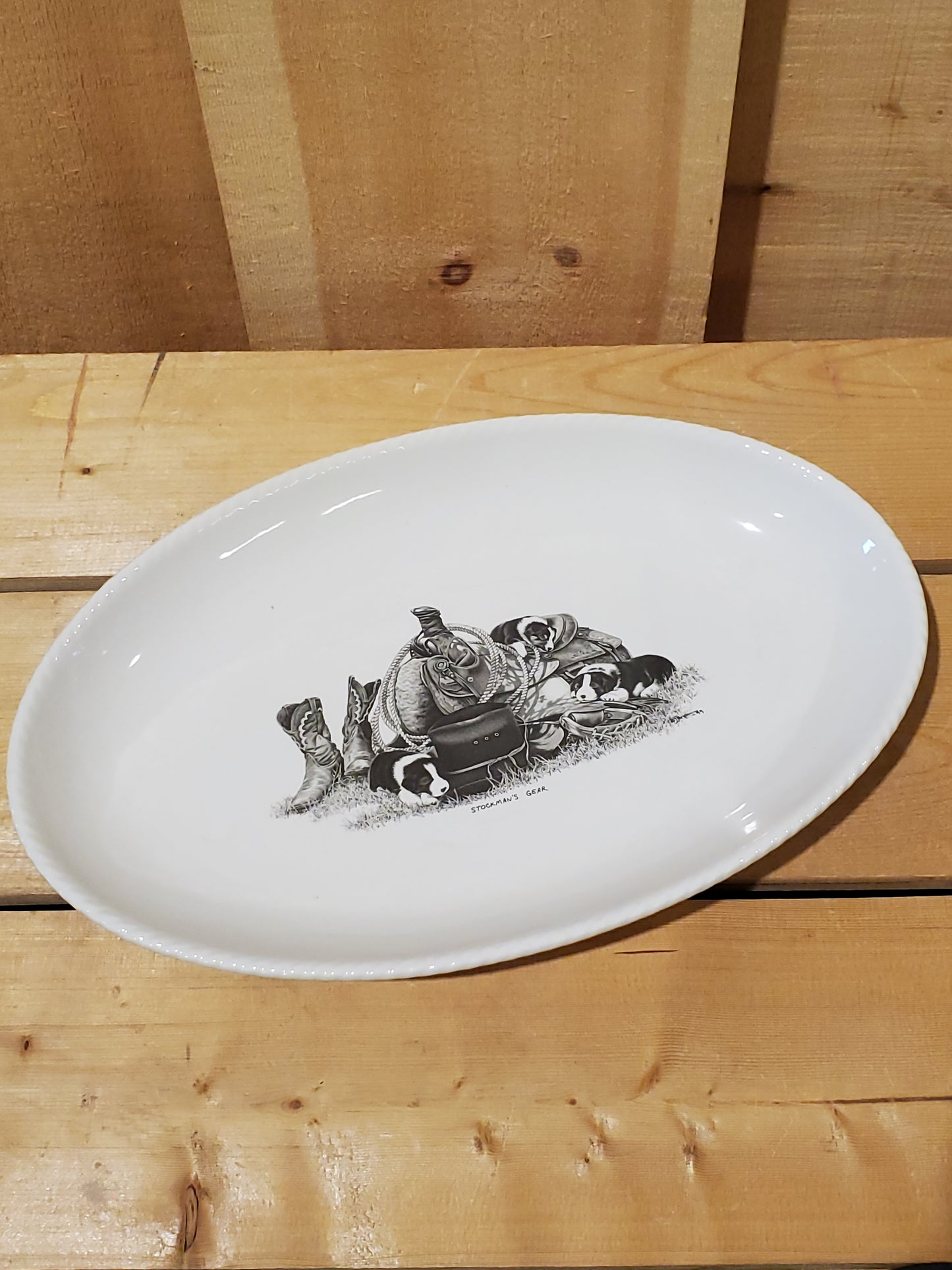 A white serving platter with a printed illustration featuring puppies on a western saddle with boots next to it.