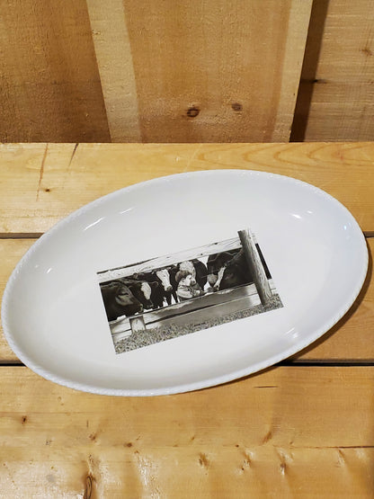 A white serving platter with a printed illustration featuring a boy feeding cows