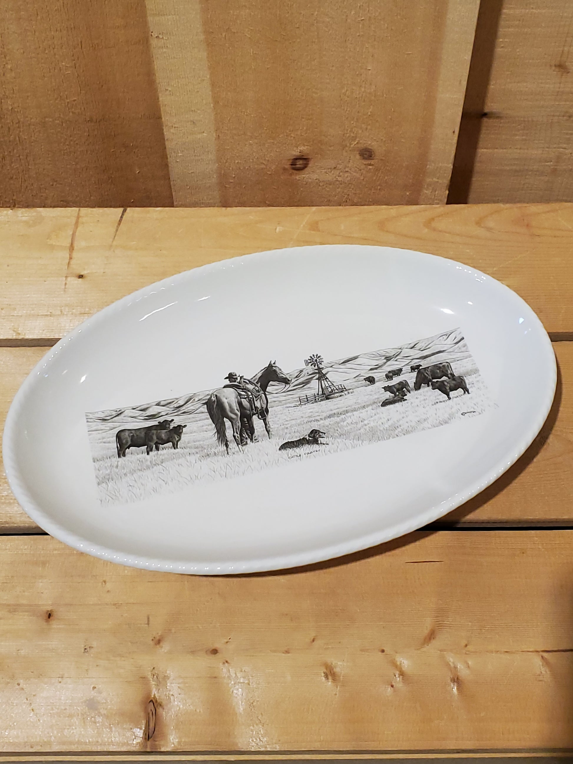A white serving platter with a printed illustration featuring a man and his horse looking at cows in a pasture
