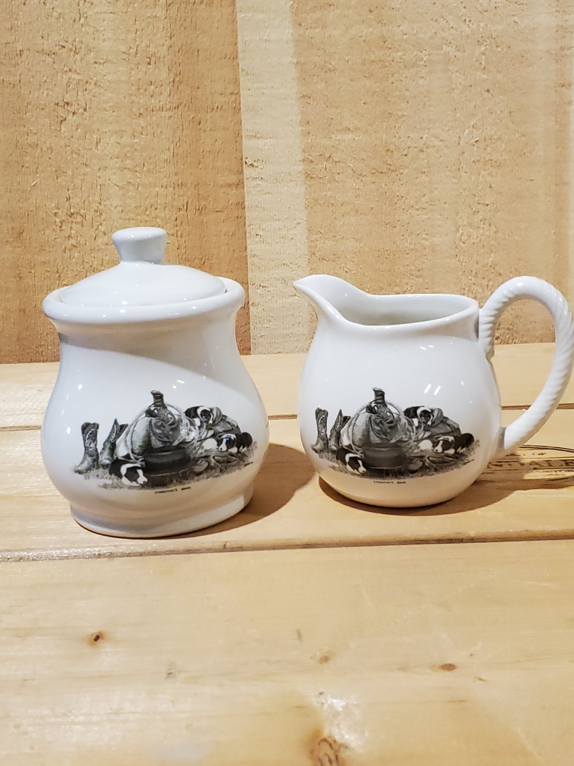 a white ceramic cream and sugar set with a black and white picture of puppies on a western saddle