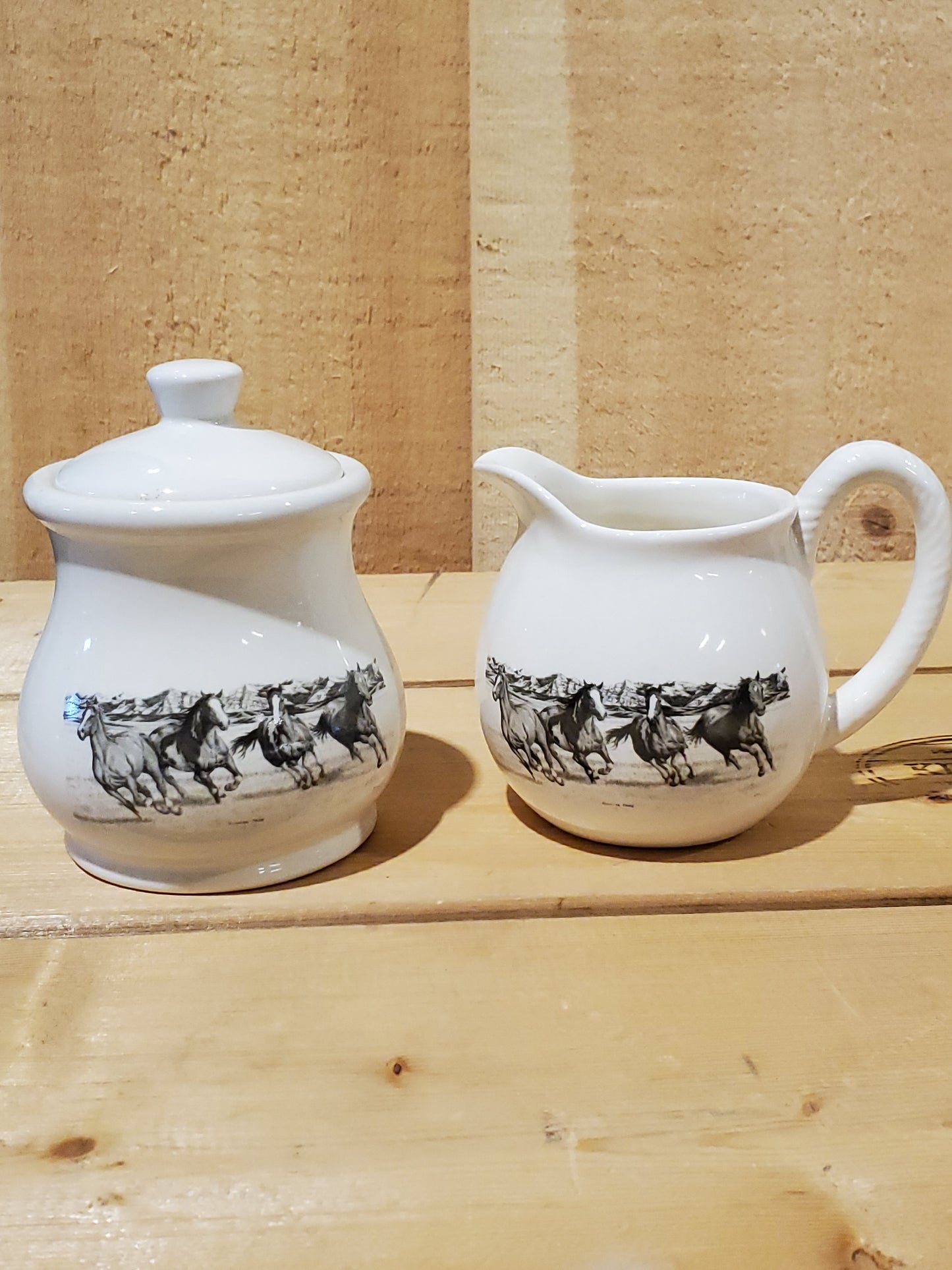 a white ceramic cream and sugar set with a black and white picture of running horses