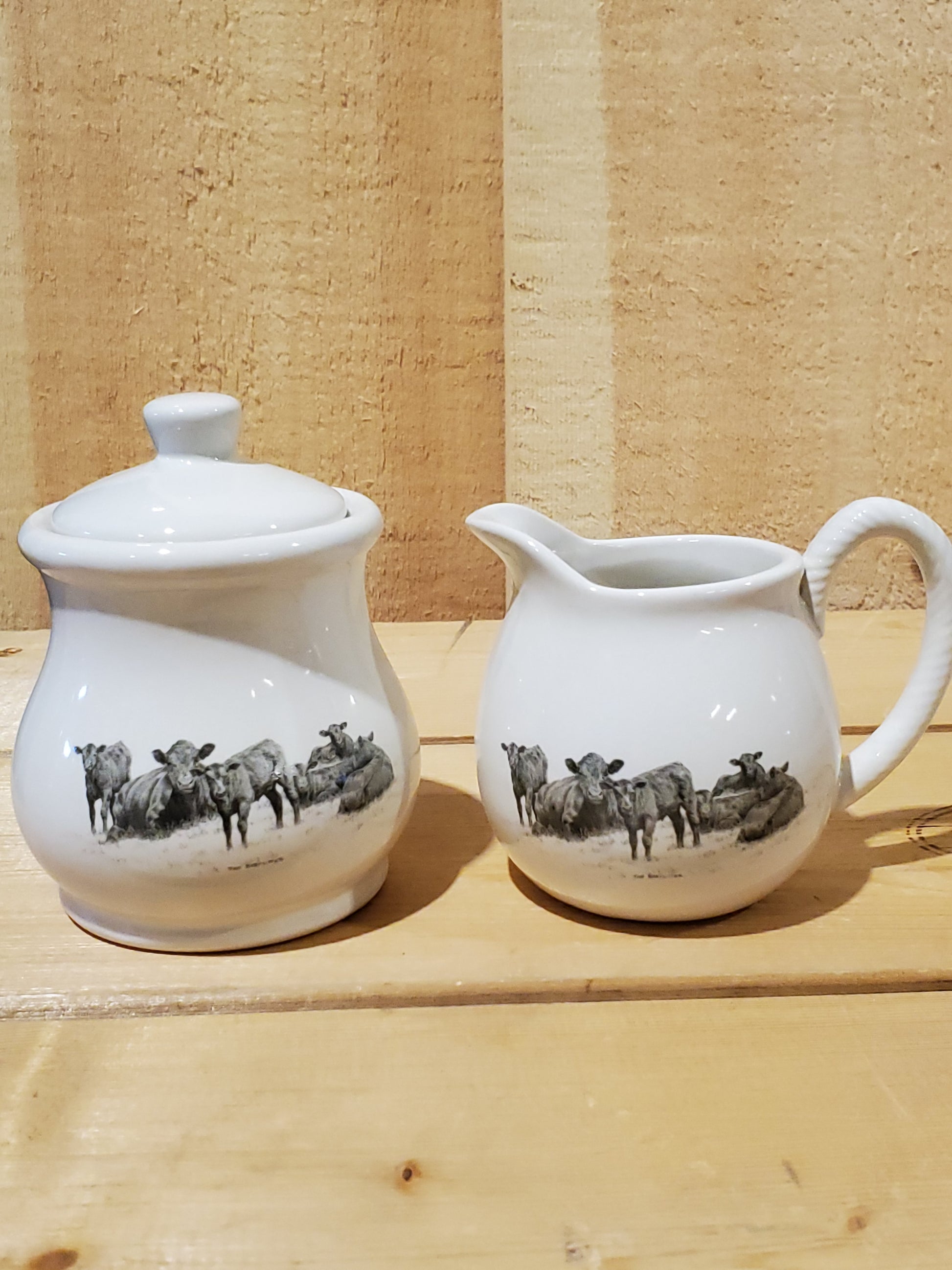 a white ceramic cream and sugar set with a black and white picture of cows resting