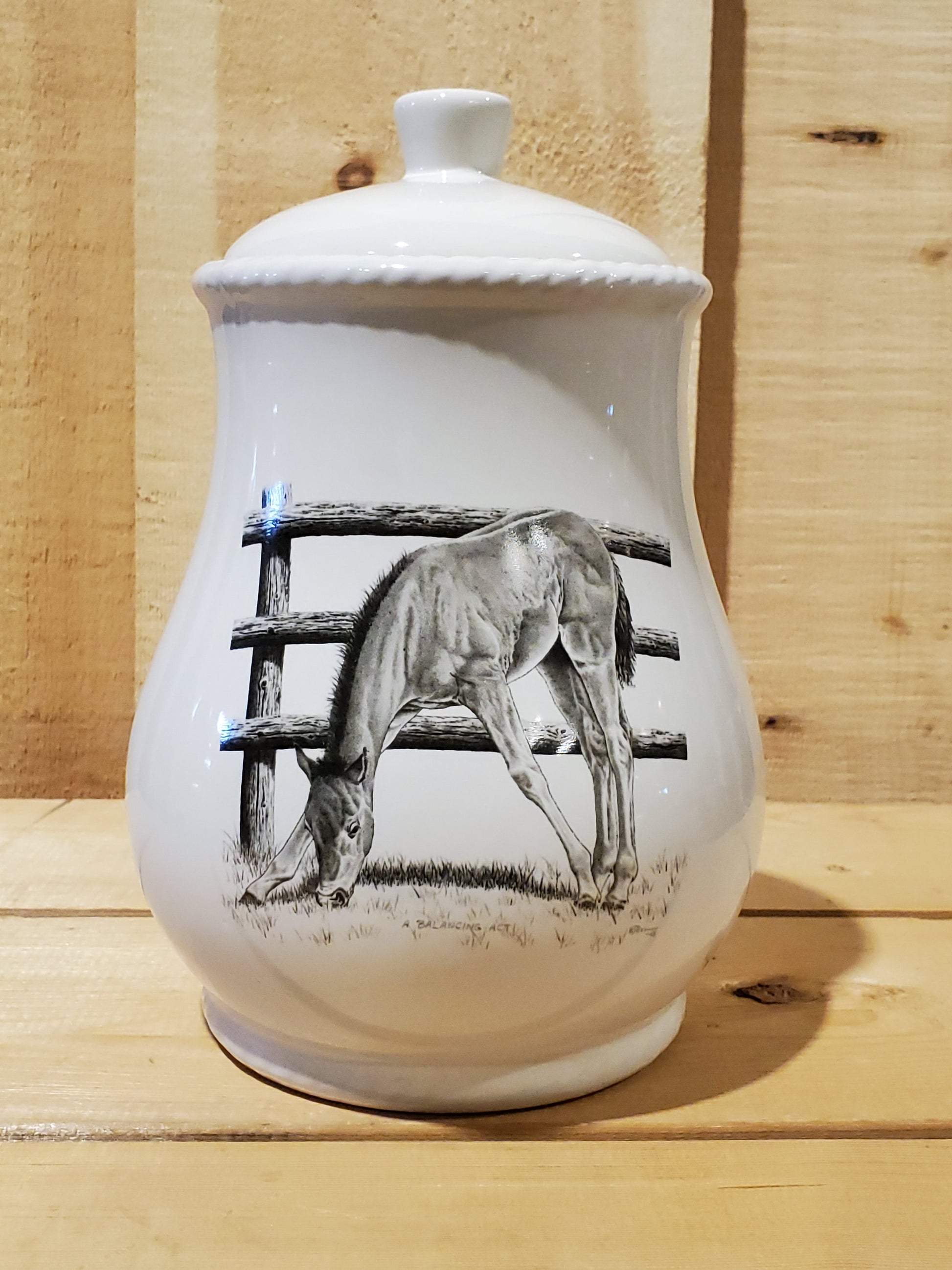 A white cookie jar with a lid, featuring a black and gray pencil art depiction of a horse and fence on the front.