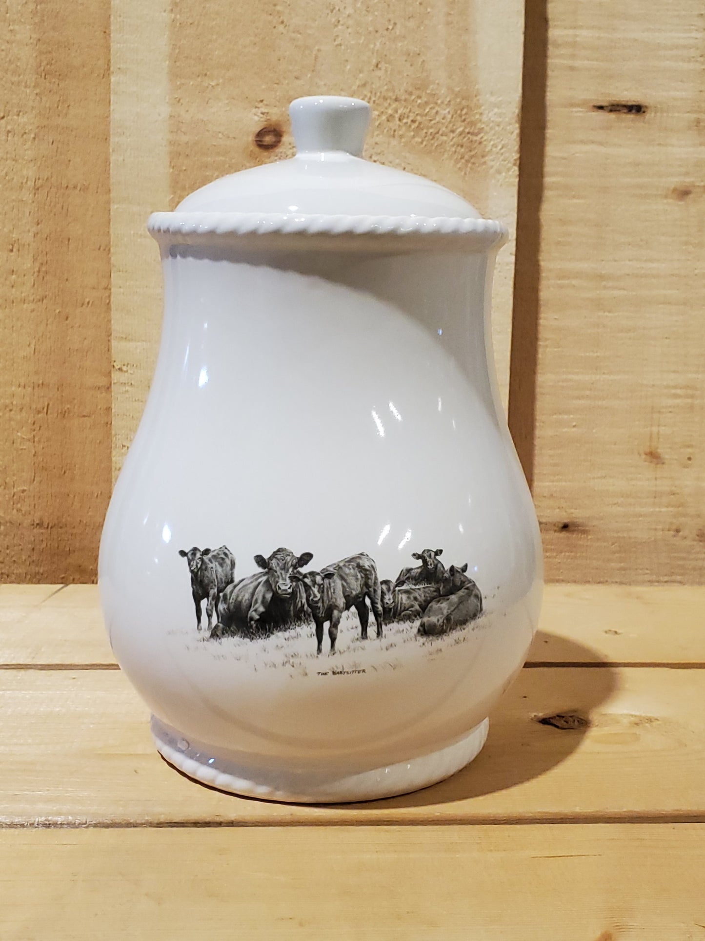 A white cookie jar with a lid, featuring a black and gray pencil art depiction of resting cows