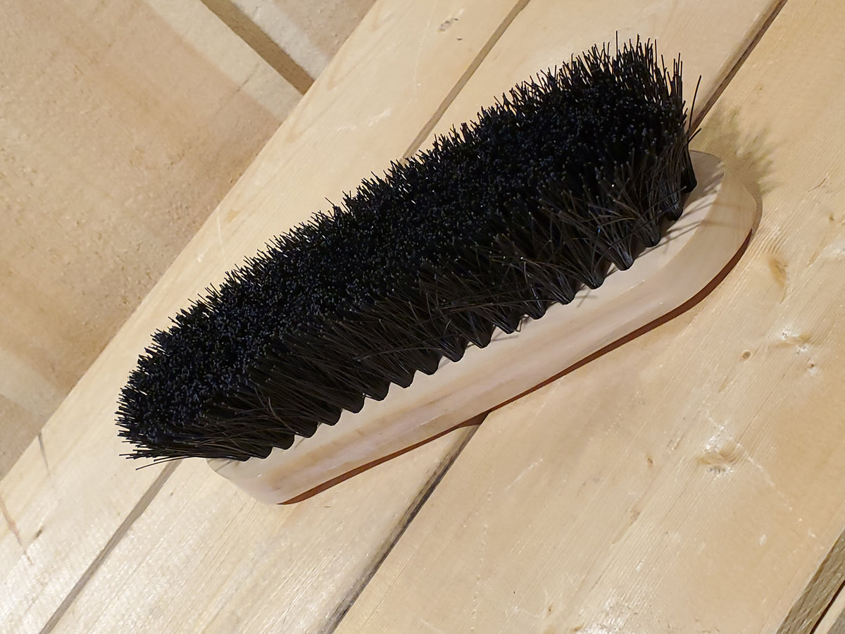 a black medium bristle dandy brush on a wooden background