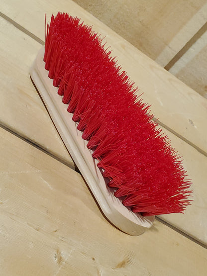 a red medium bristle dandy brush on a wooden background