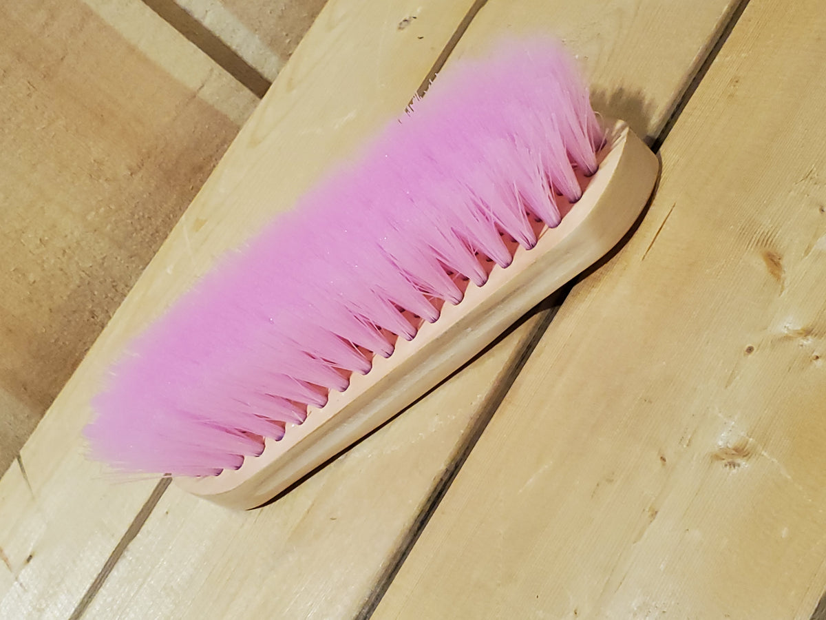 a pink medium bristle dandy brush on a wooden background