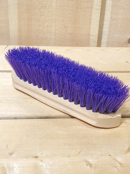 a purple hard bristled wooden handle dandy brush for horses on a wooden background