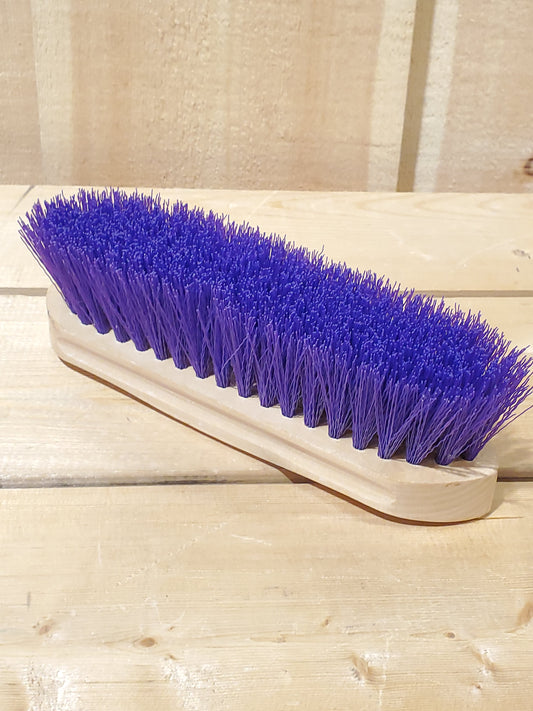 a purple hard bristled wooden handle dandy brush for horses on a wooden background