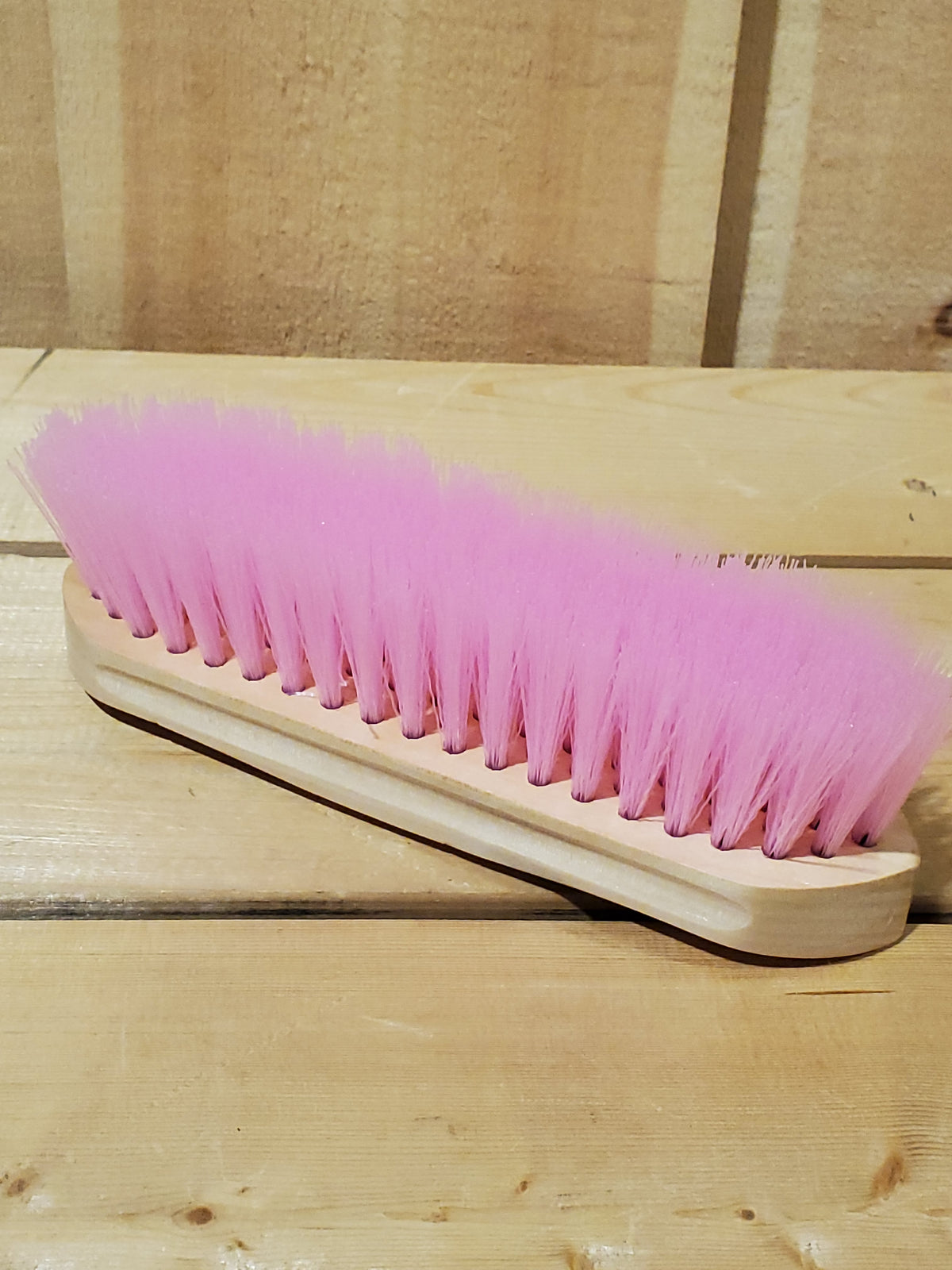a pink hard bristled wooden handle dandy brush for horses on a wooden background