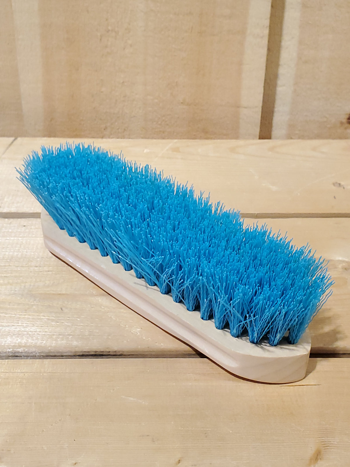 a teal hard bristled wooden handle dandy brush for horses on a wooden background