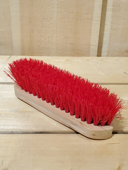 a red hard bristled wooden handle dandy brush for horses on a wooden background