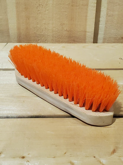 an orange hard bristled wooden handle dandy brush for horses on a wooden background