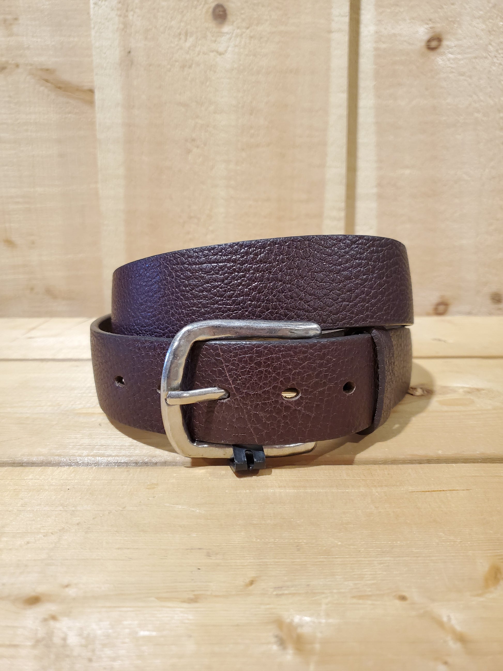A brown leather men's belt with a buckle, displayed on a wooden background.