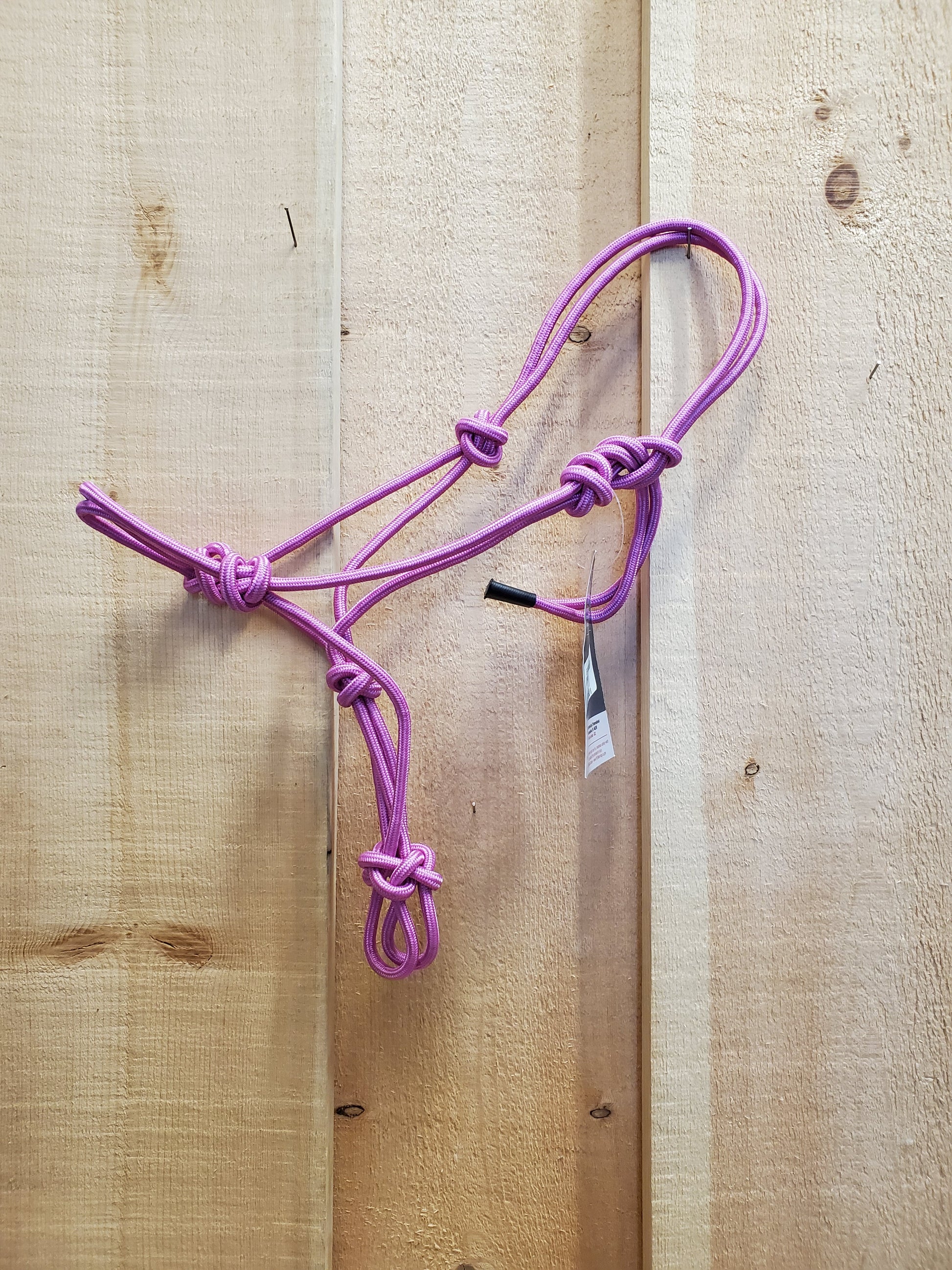A light pink poly-nylon rope halter hanging against a wooden 