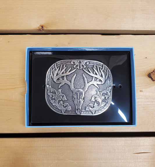 A belt buckle with a smooth edge and a buck skull design, presented in an antique finish, displayed on a wooden surface.