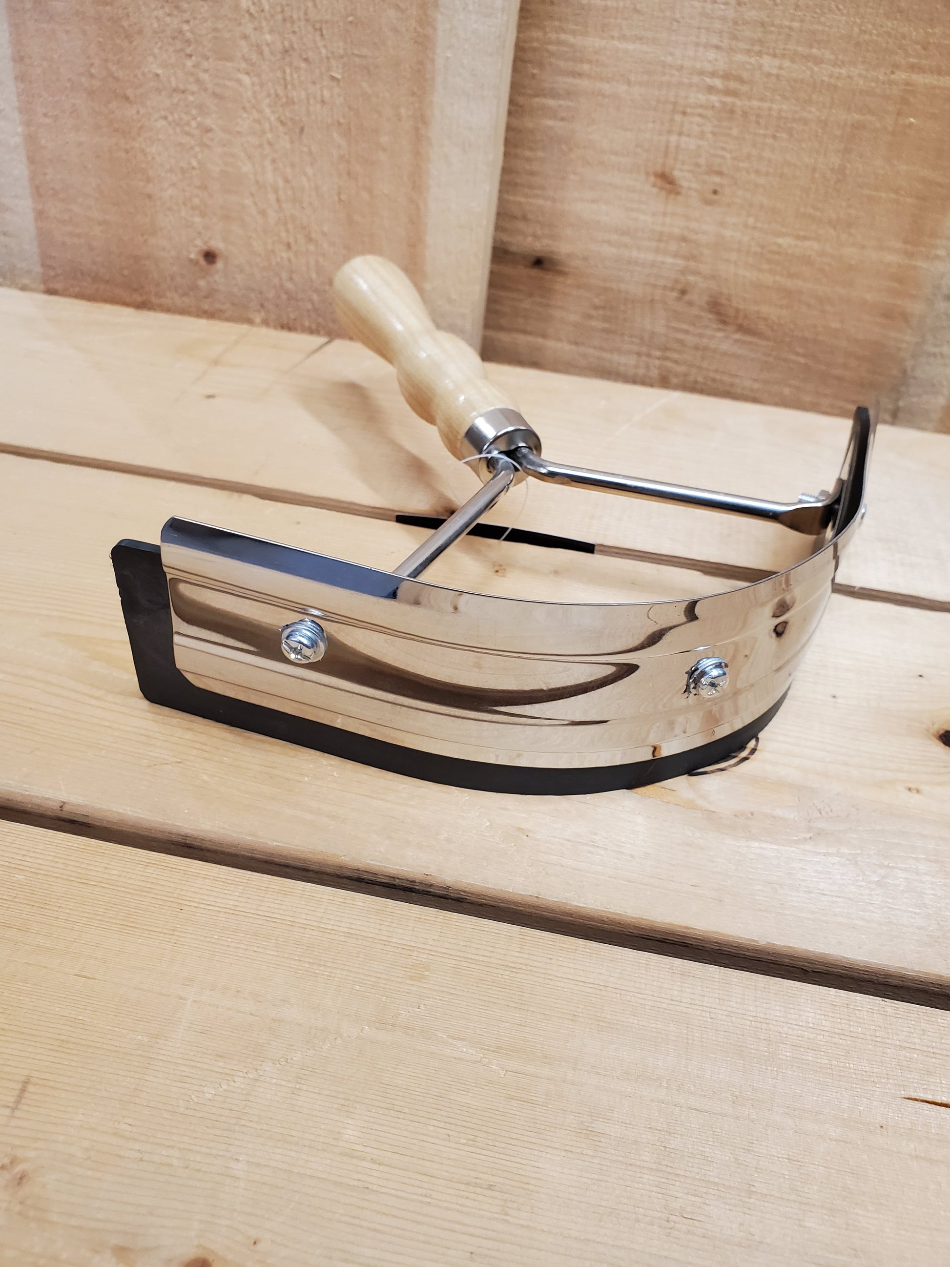 A sweat scraper with a rubber blade and a wooden handle positioned on a wooden surface.