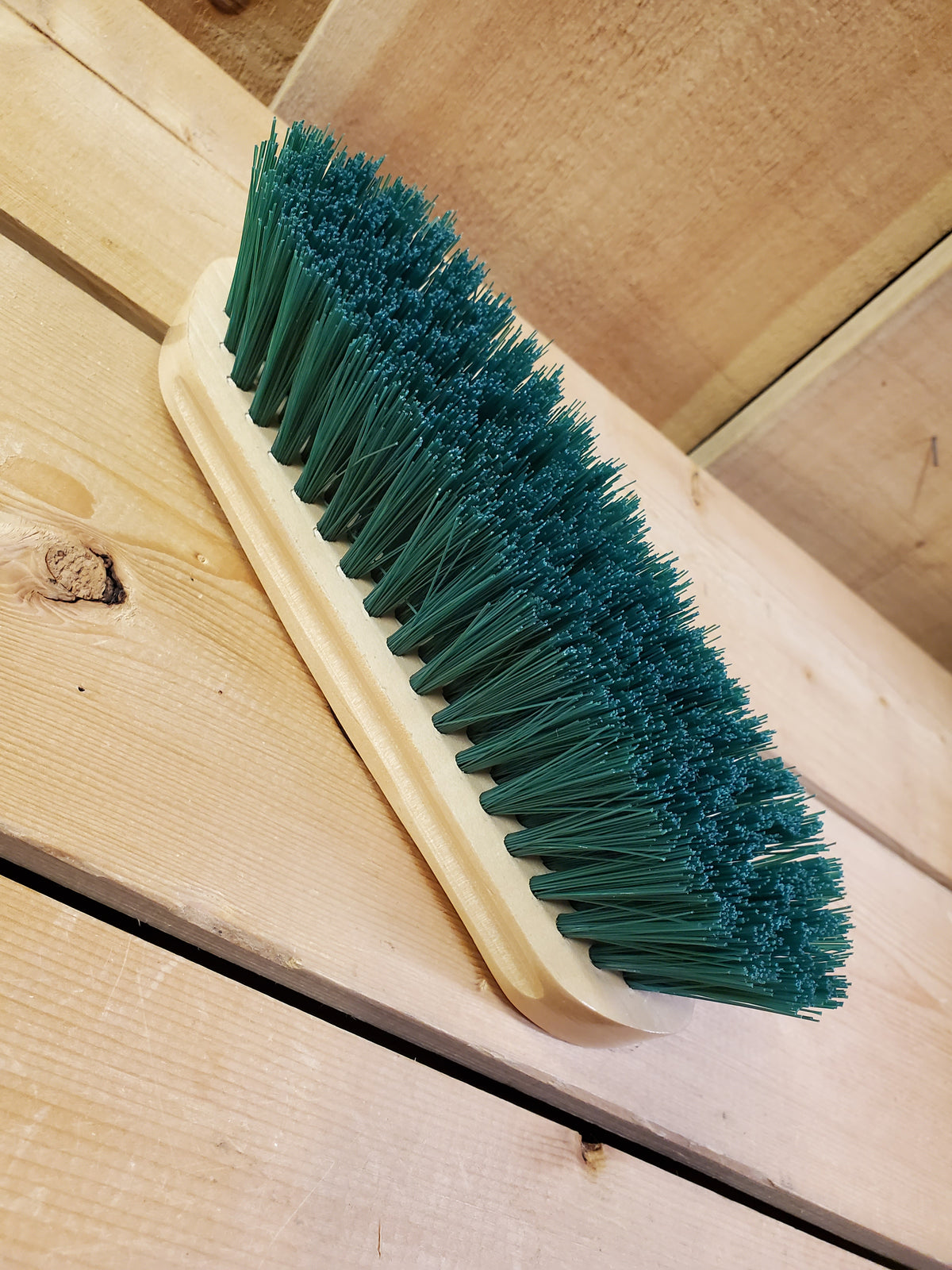 a green medium bristle dandy brush on a wooden background