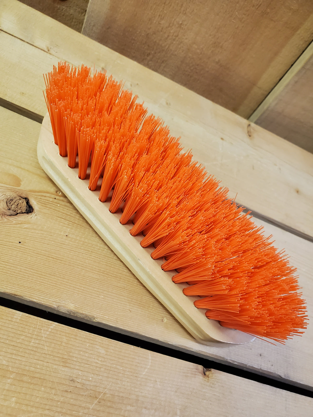 an orange medium bristle dandy brush on a wooden background