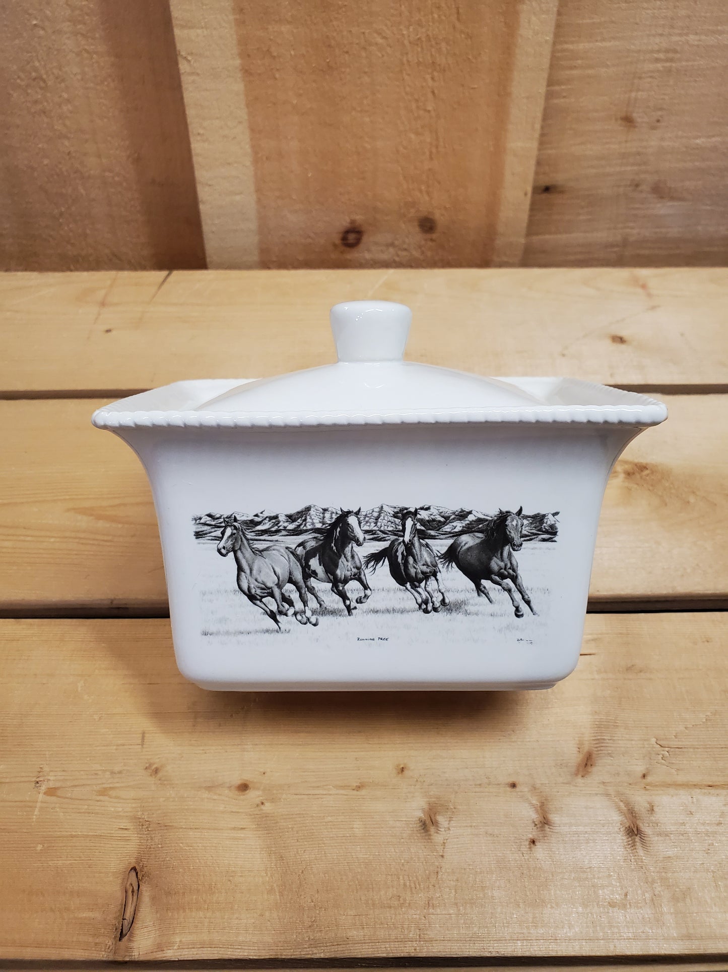 A white ceramic butter dish with a lid, featuring a black and white illustration of running horses