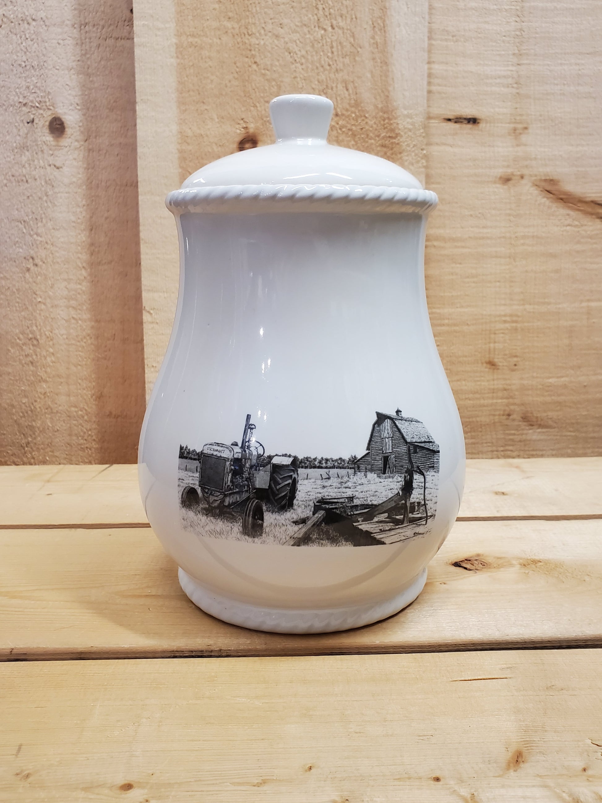 A white cookie jar with a lid, featuring a black and gray pencil art depiction of an old farmstead