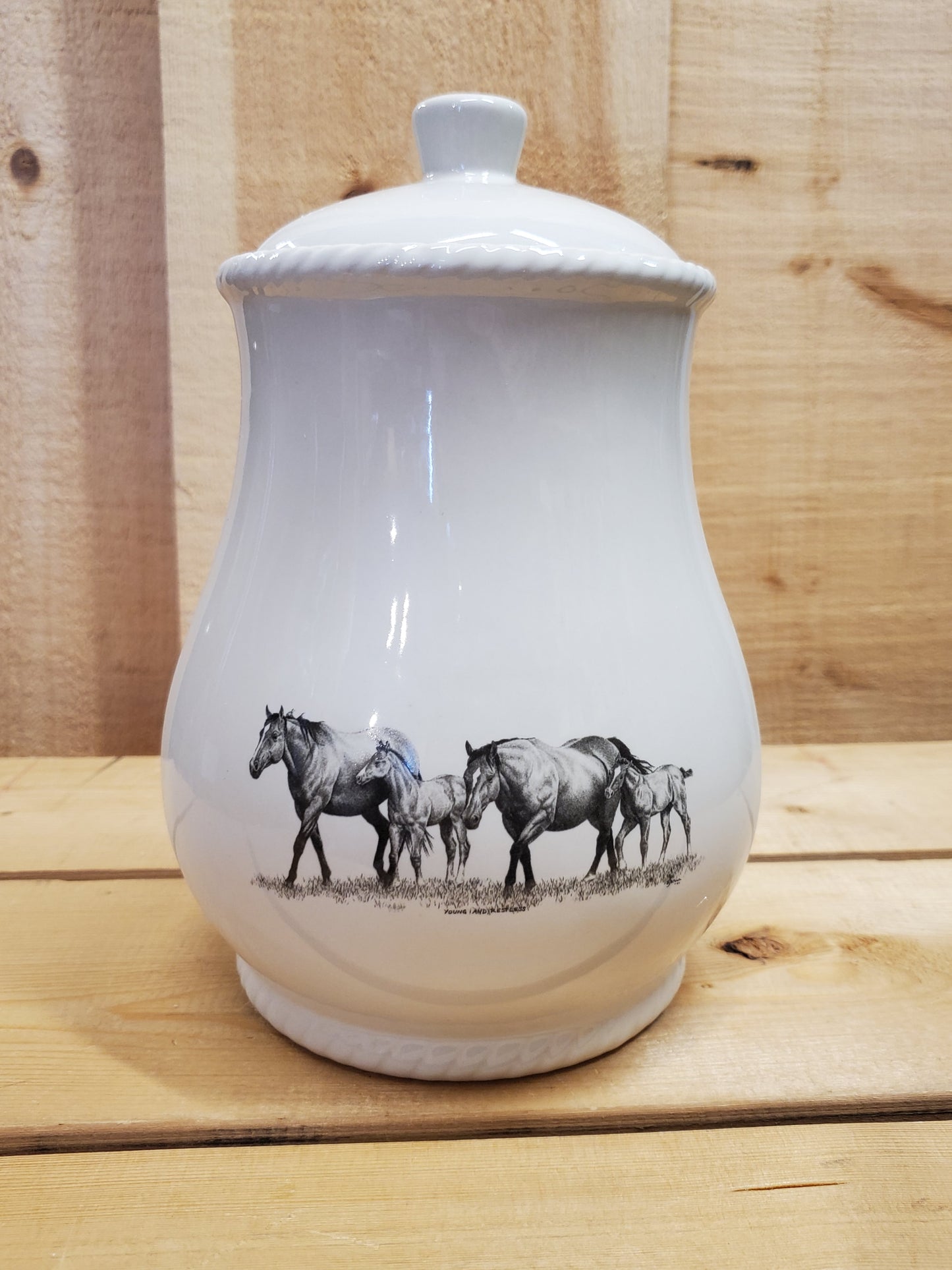 A white cookie jar with a lid, featuring a black and gray pencil art depiction of two mares and two foals