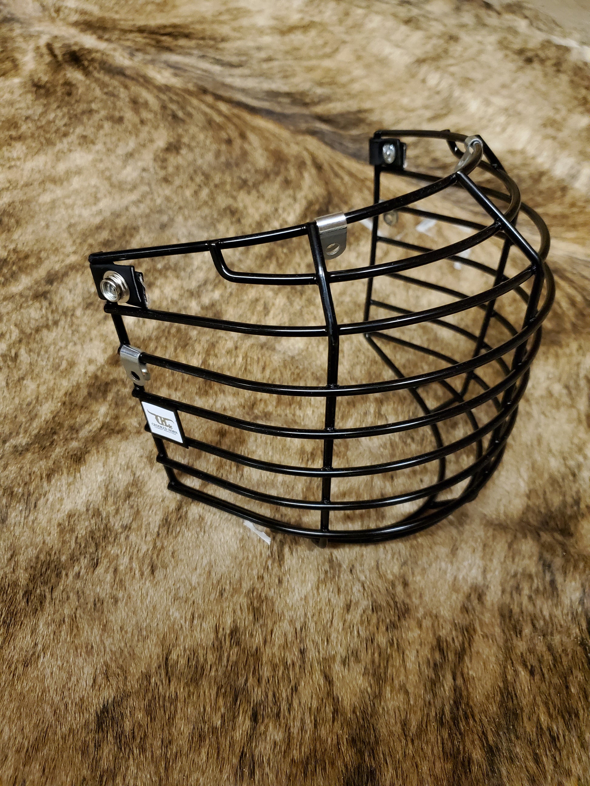 A black crooked horn helmet cage placed on a textured surface, presumably a part of bull riding gear.