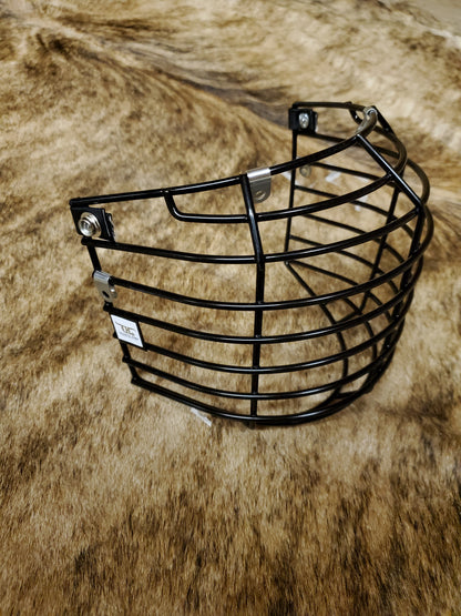 A black crooked horn helmet cage placed on a textured surface, presumably a part of bull riding gear.