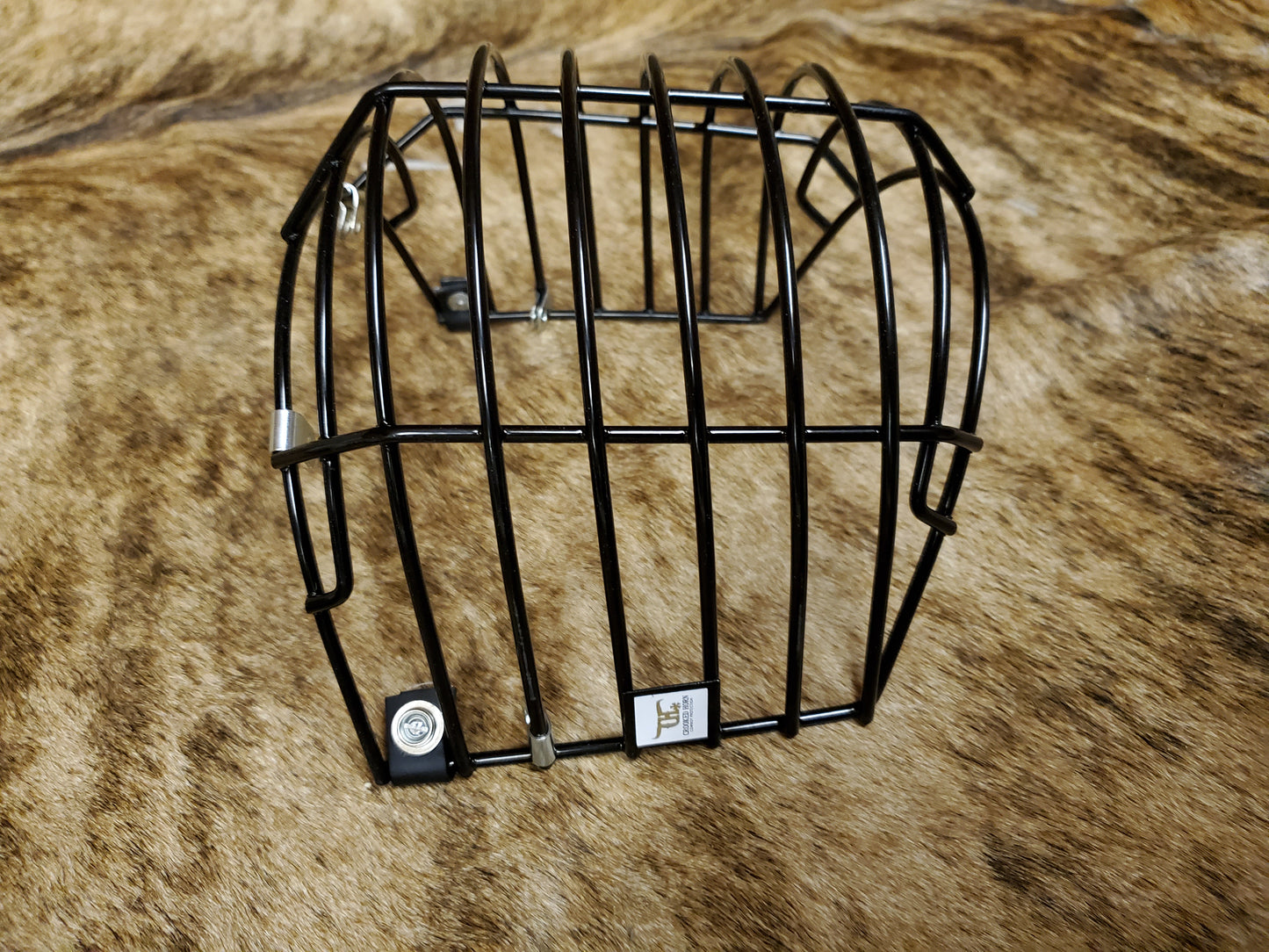 A black crooked horn helmet cage placed on a textured surface, presumably a part of bull riding gear.