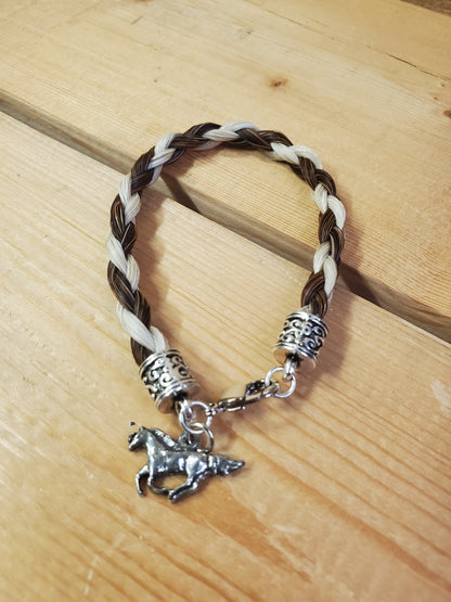 a braided horsehair bracelet with a horse charm on a wooden background