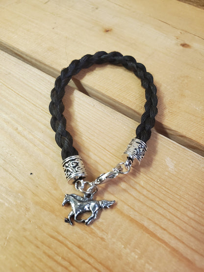 a braided horsehair bracelet with a horse charm on a wooden background