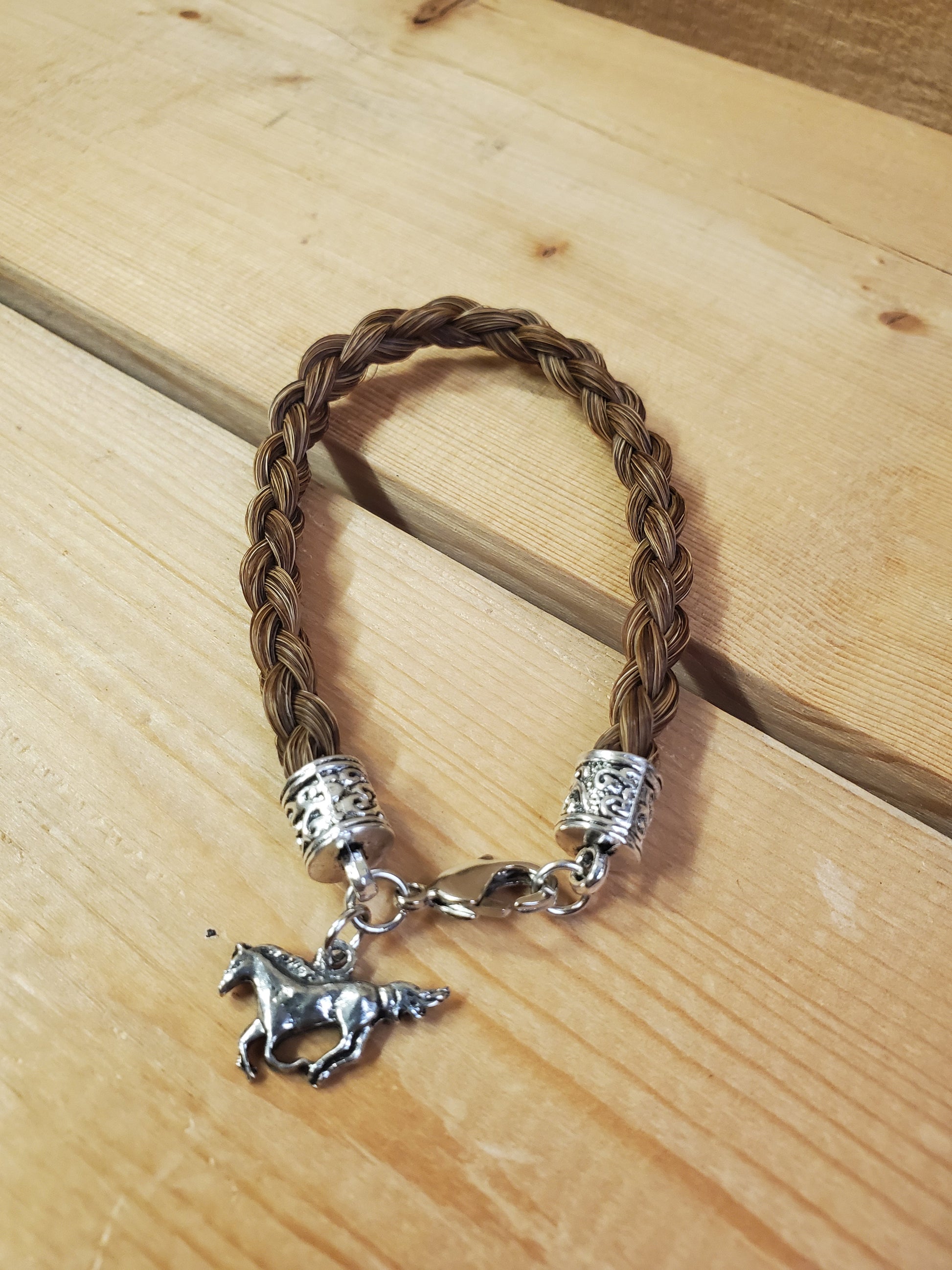 a braided horsehair bracelet with a horse charm on a wooden background