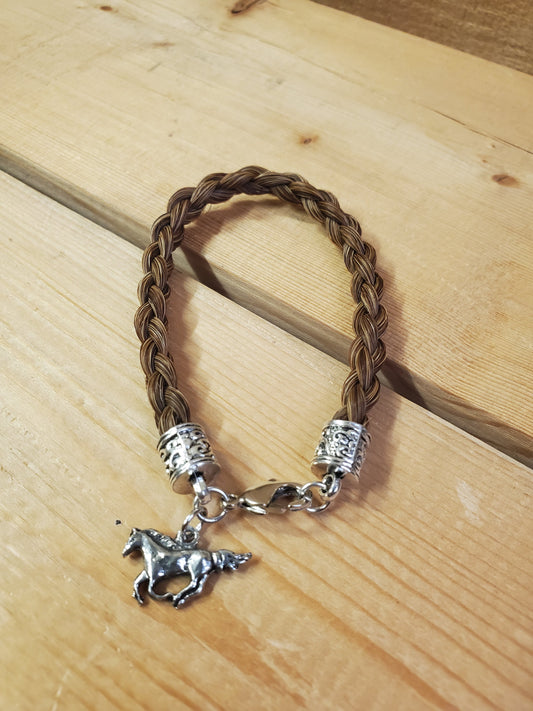 a braided horsehair bracelet with a horse charm on a wooden background
