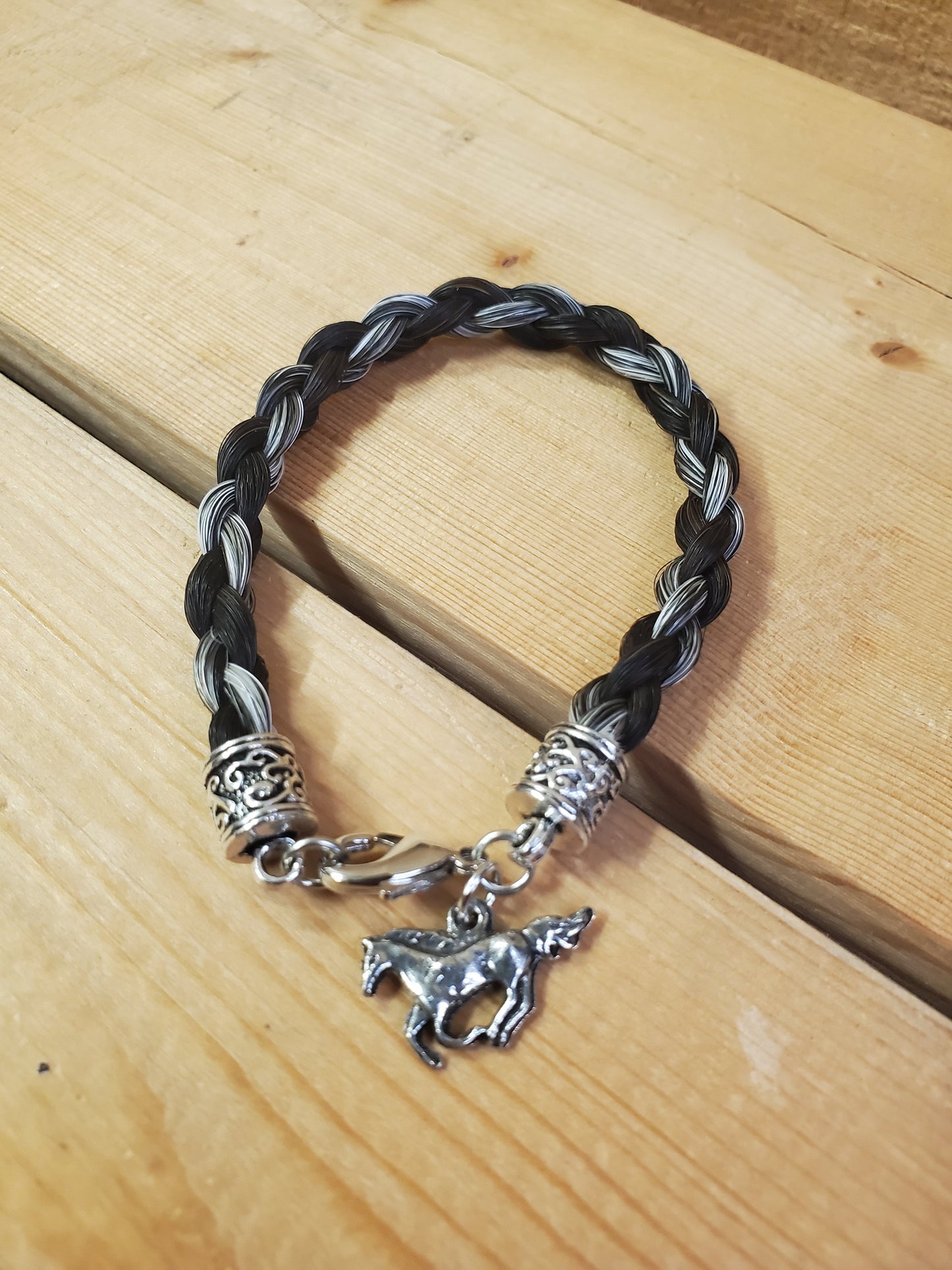 a braided horsehair bracelet with a horse charm on a wooden background