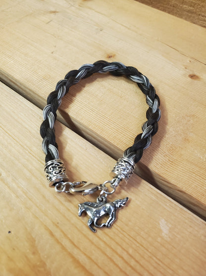a braided horsehair bracelet with a horse charm on a wooden background