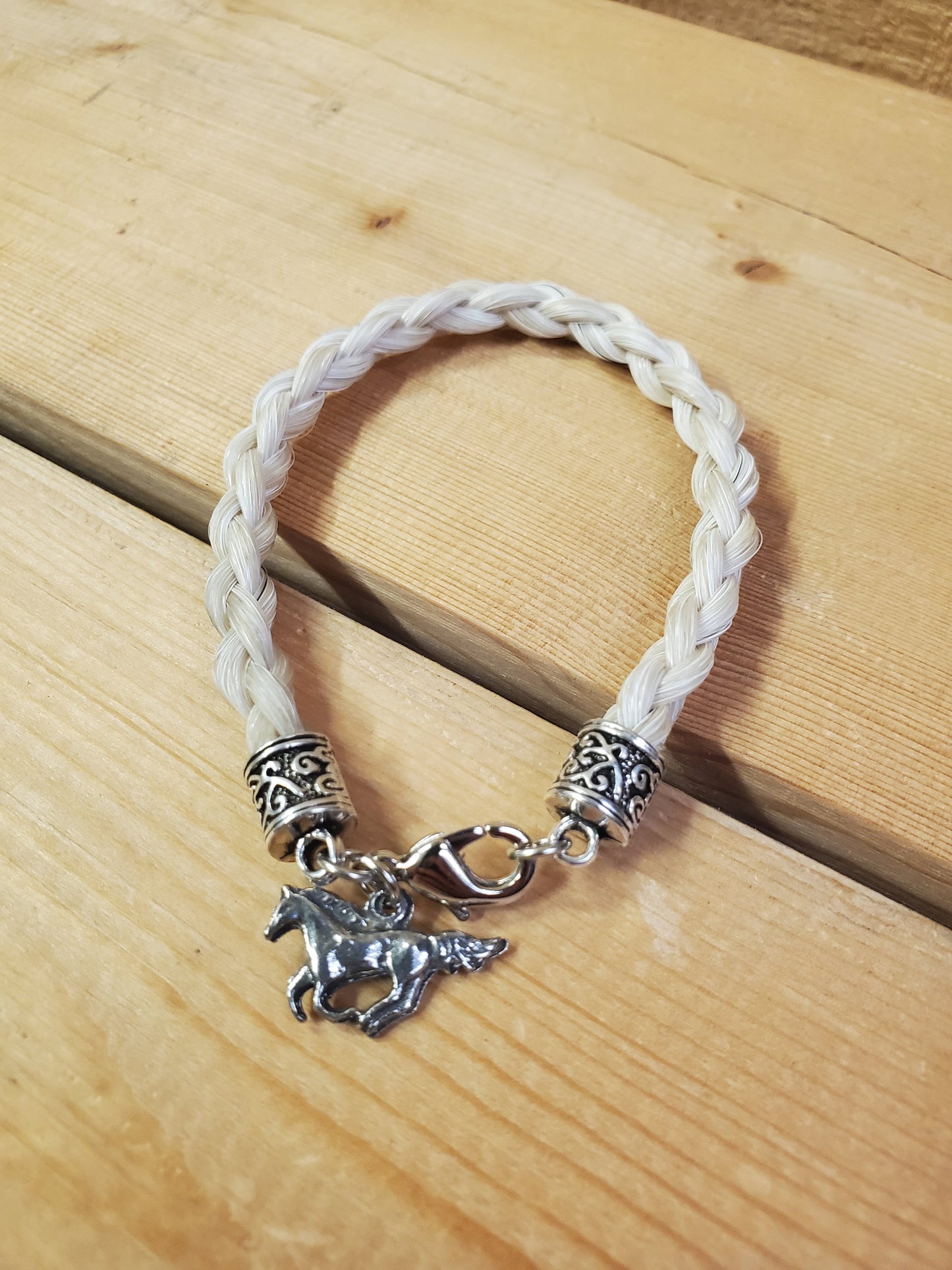a braided horsehair bracelet with a horse charm on a wooden background