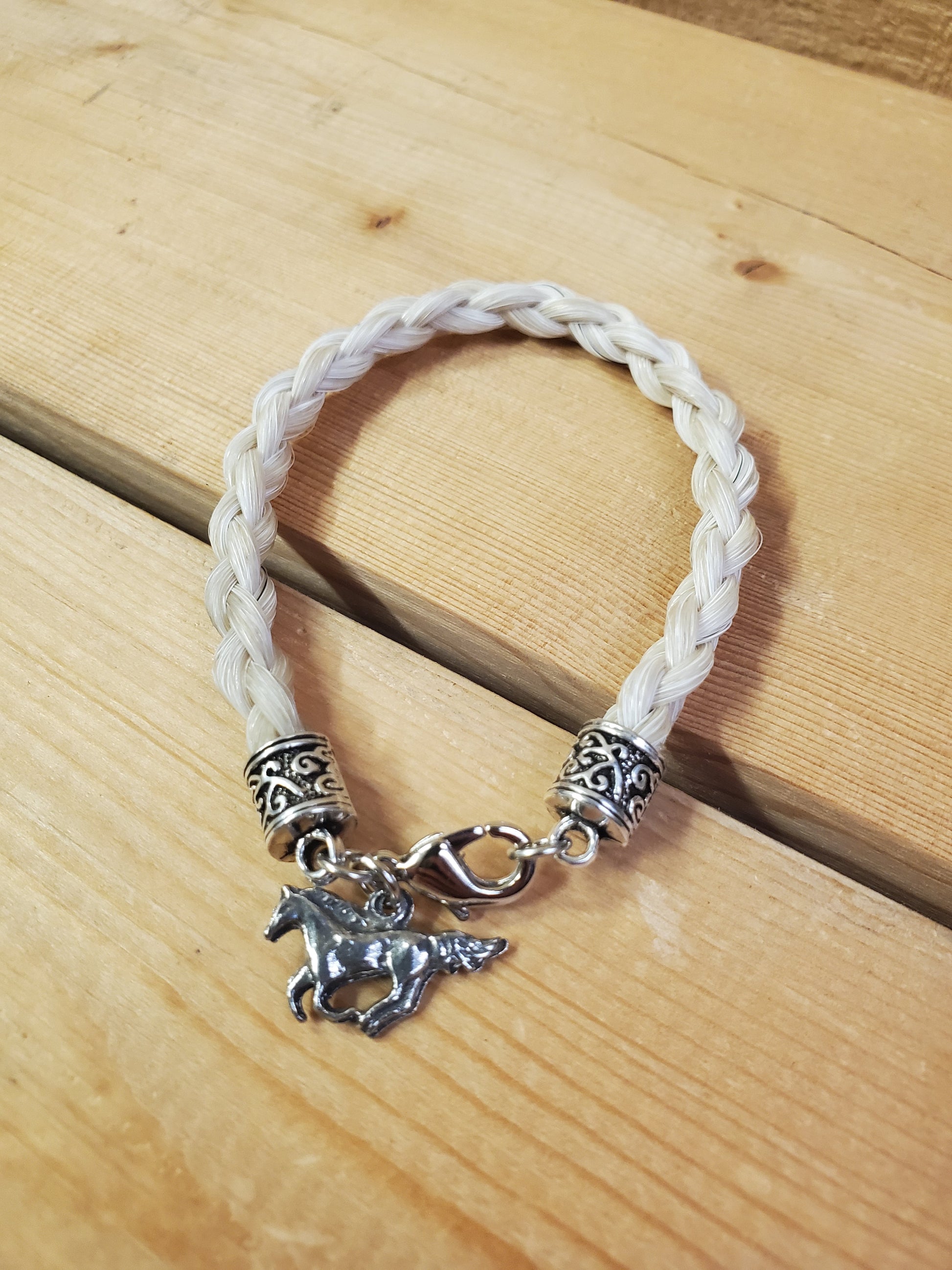 a braided horsehair bracelet with a horse charm on a wooden background