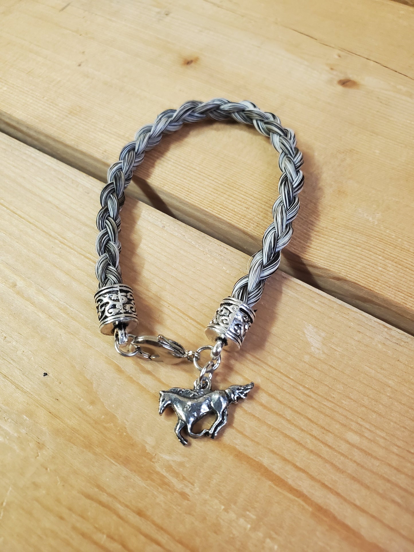 a braided horsehair bracelet with a horse charm on a wooden background