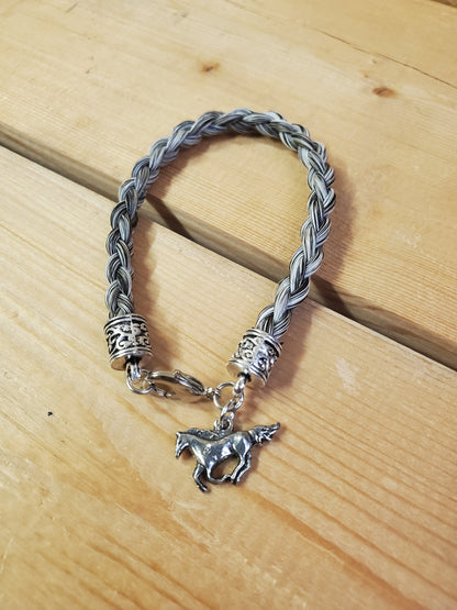 a braided horsehair bracelet with a horse charm on a wooden background
