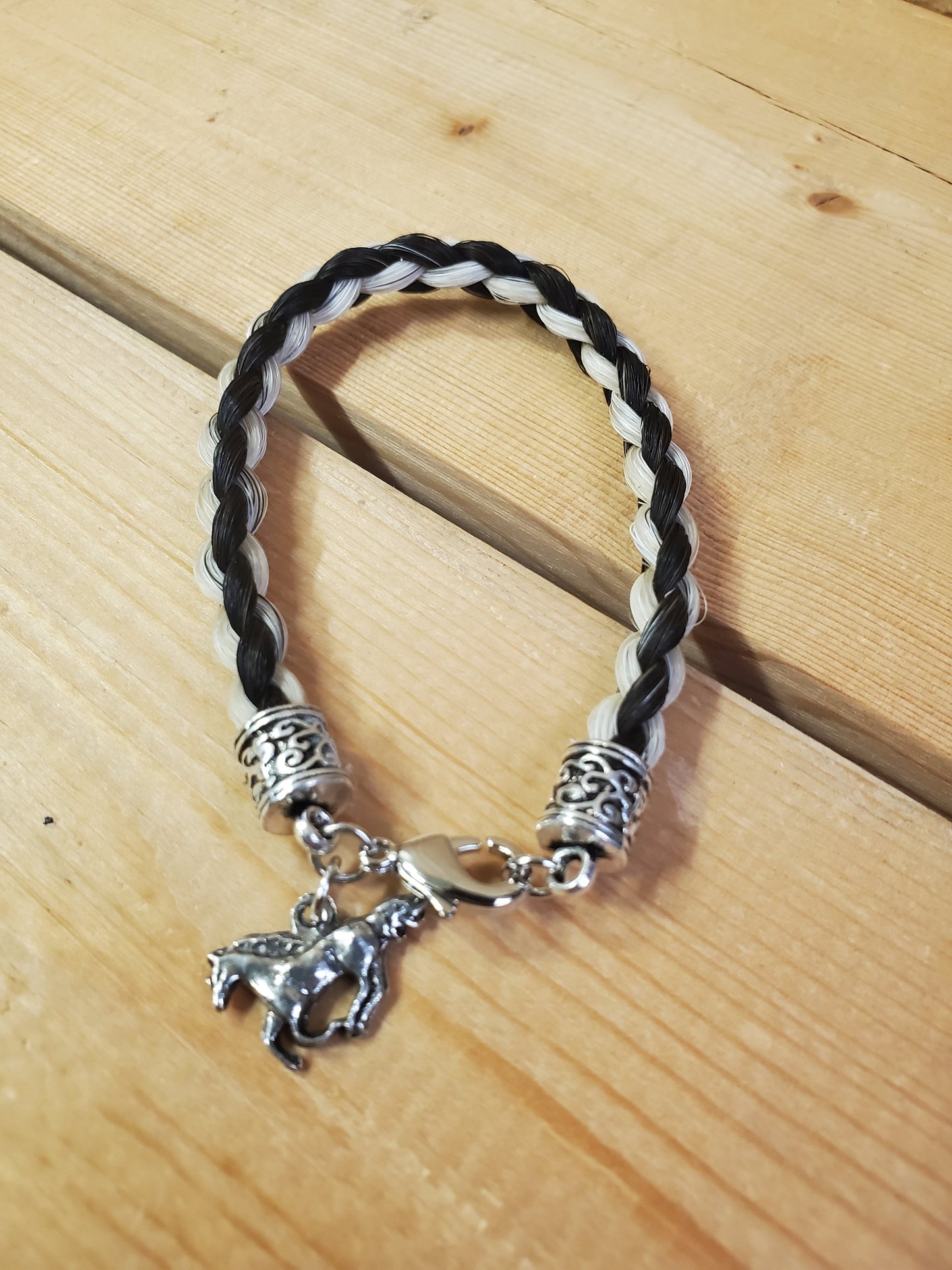 a braided horsehair bracelet with a horse charm on a wooden background