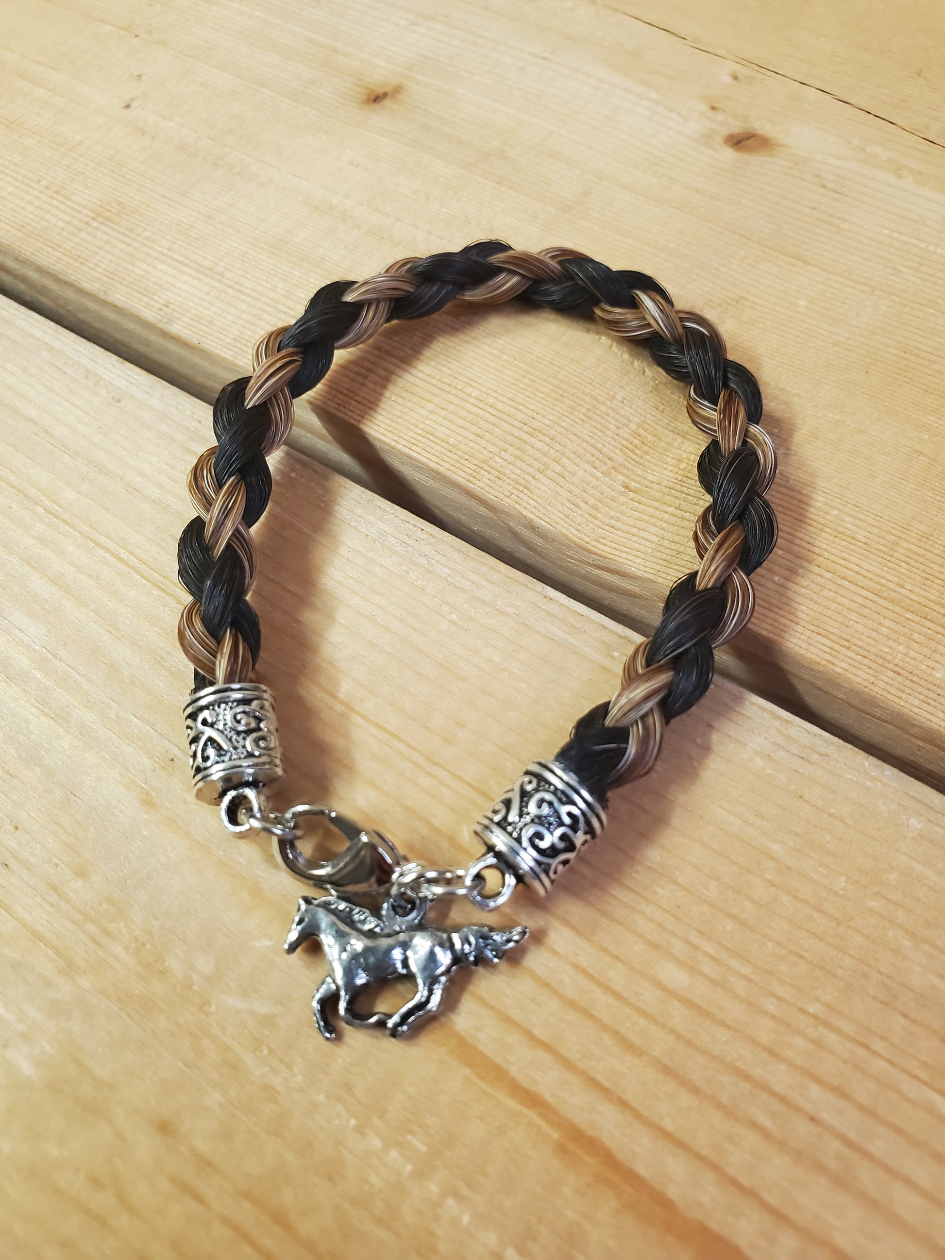 a braided horsehair bracelet with a horse charm on a wooden background