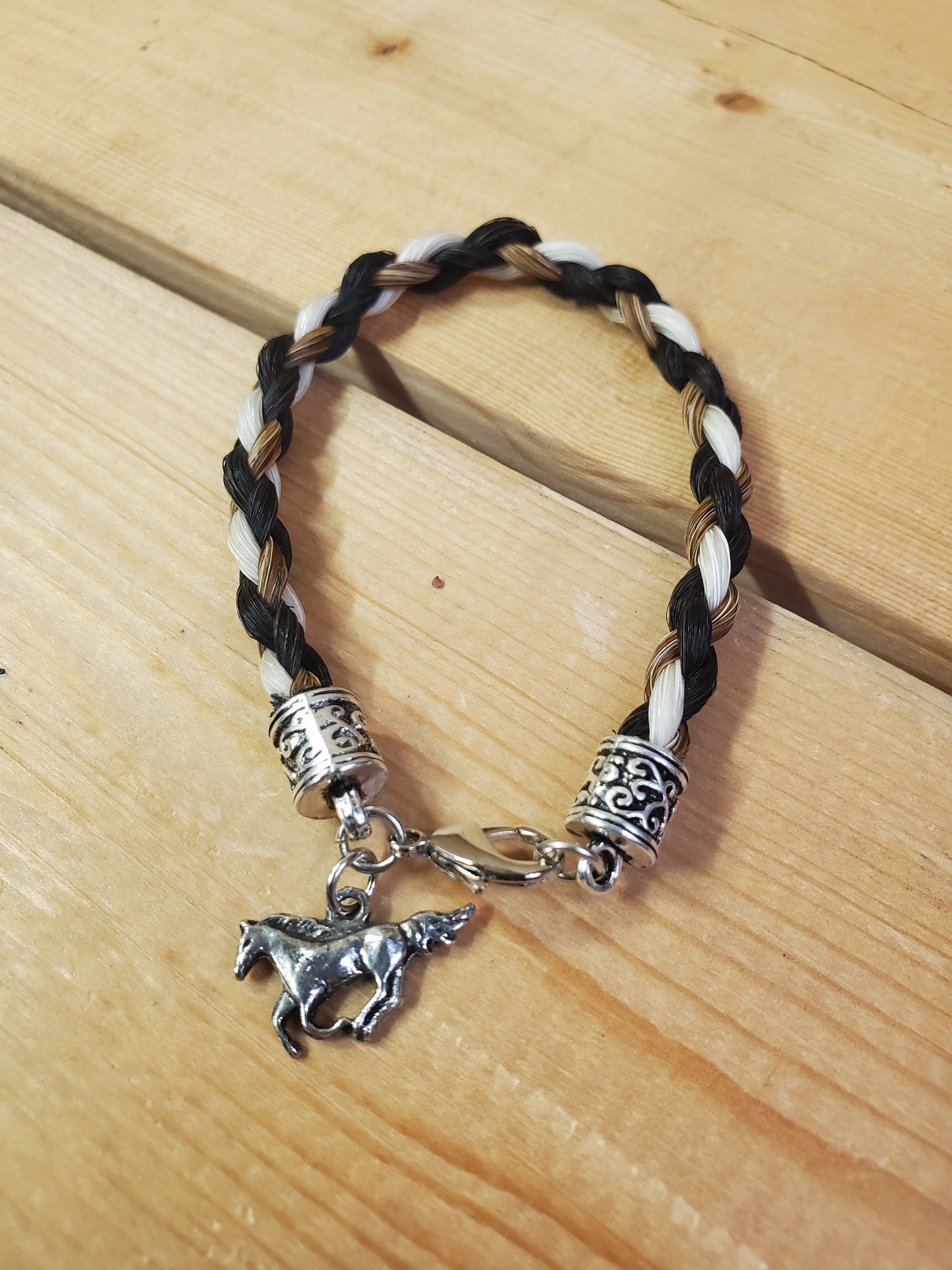 a braided horsehair bracelet with a horse charm on a wooden background
