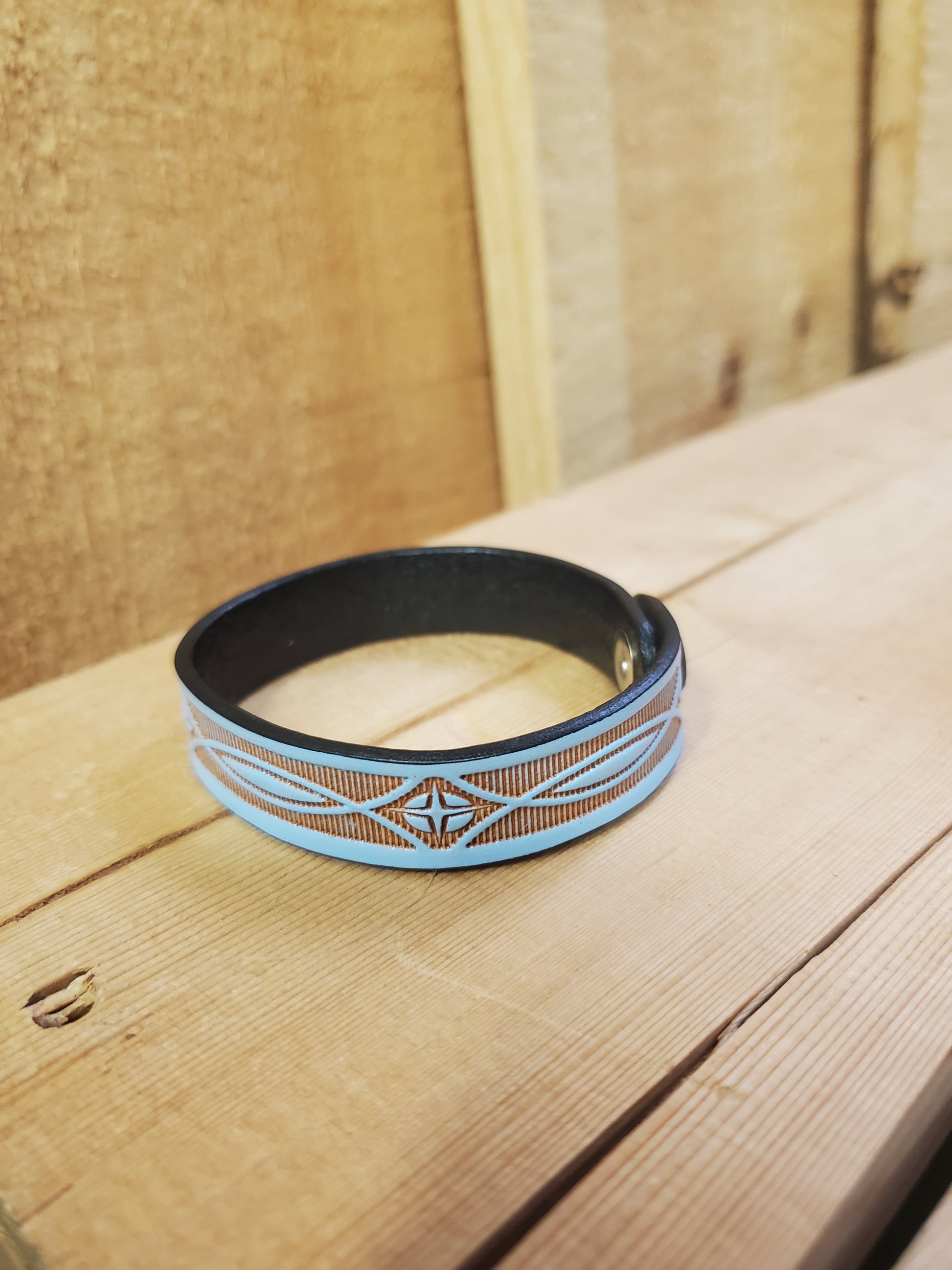 A blue leather bracelet with a stamped pattern, displayed on a wooden surface.