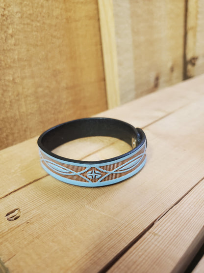 A blue leather bracelet with a stamped pattern, displayed on a wooden surface.