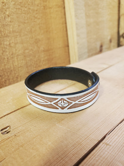 A white leather bracelet with a stamped pattern, displayed on a wooden surface.