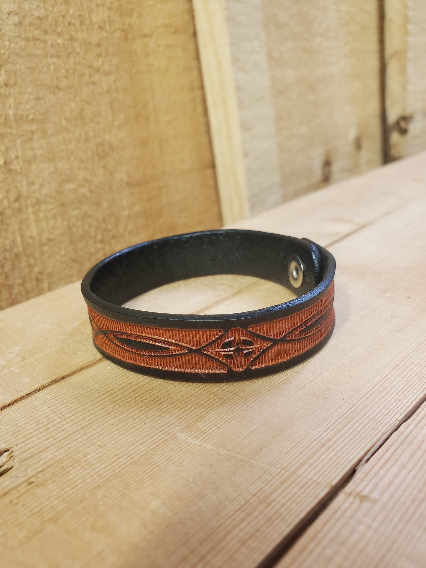 A brown leather bracelet with a stamped pattern, displayed on a wooden surface.