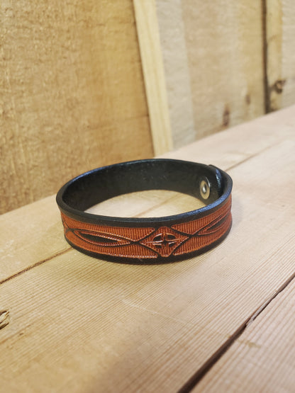 A brown leather bracelet with a stamped pattern, displayed on a wooden surface.