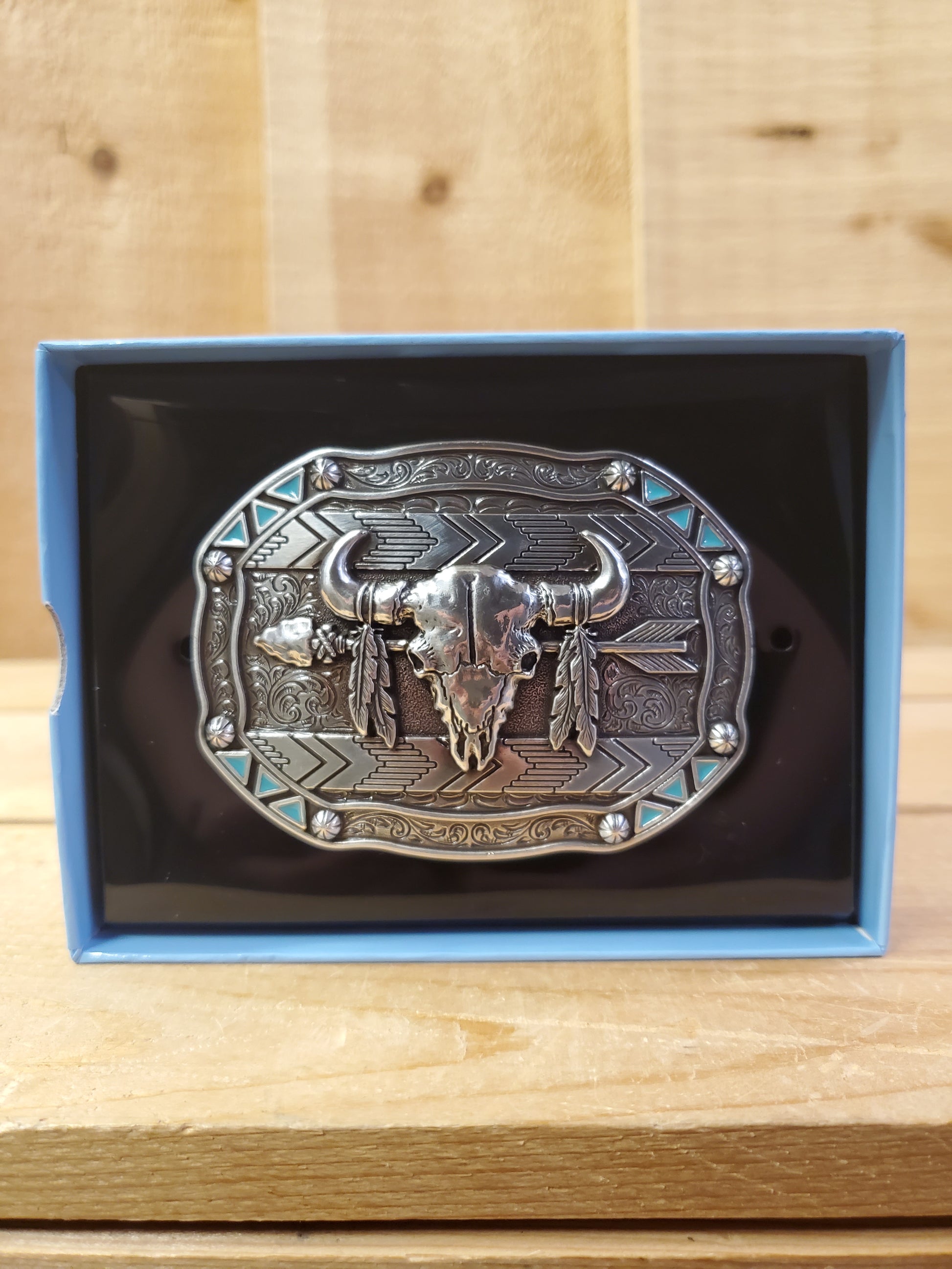 A belt buckle with a bison skull design, presented on a blue and black card with a wooden background.