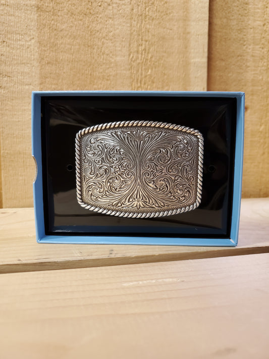 A belt buckle with scrollwork and rope edge detail, displayed in an open box with a blue interior.