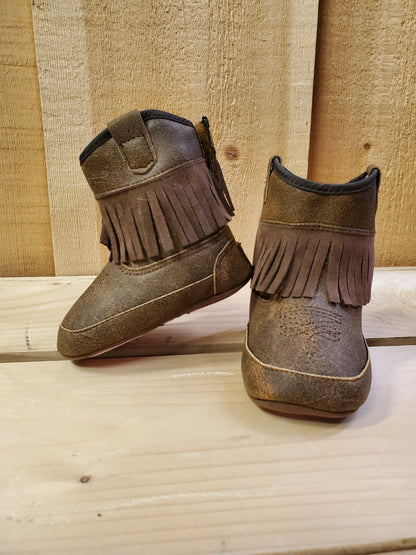 A pair of brown baby buckers with fringe detail on the side, displayed against a wooden backdrop.